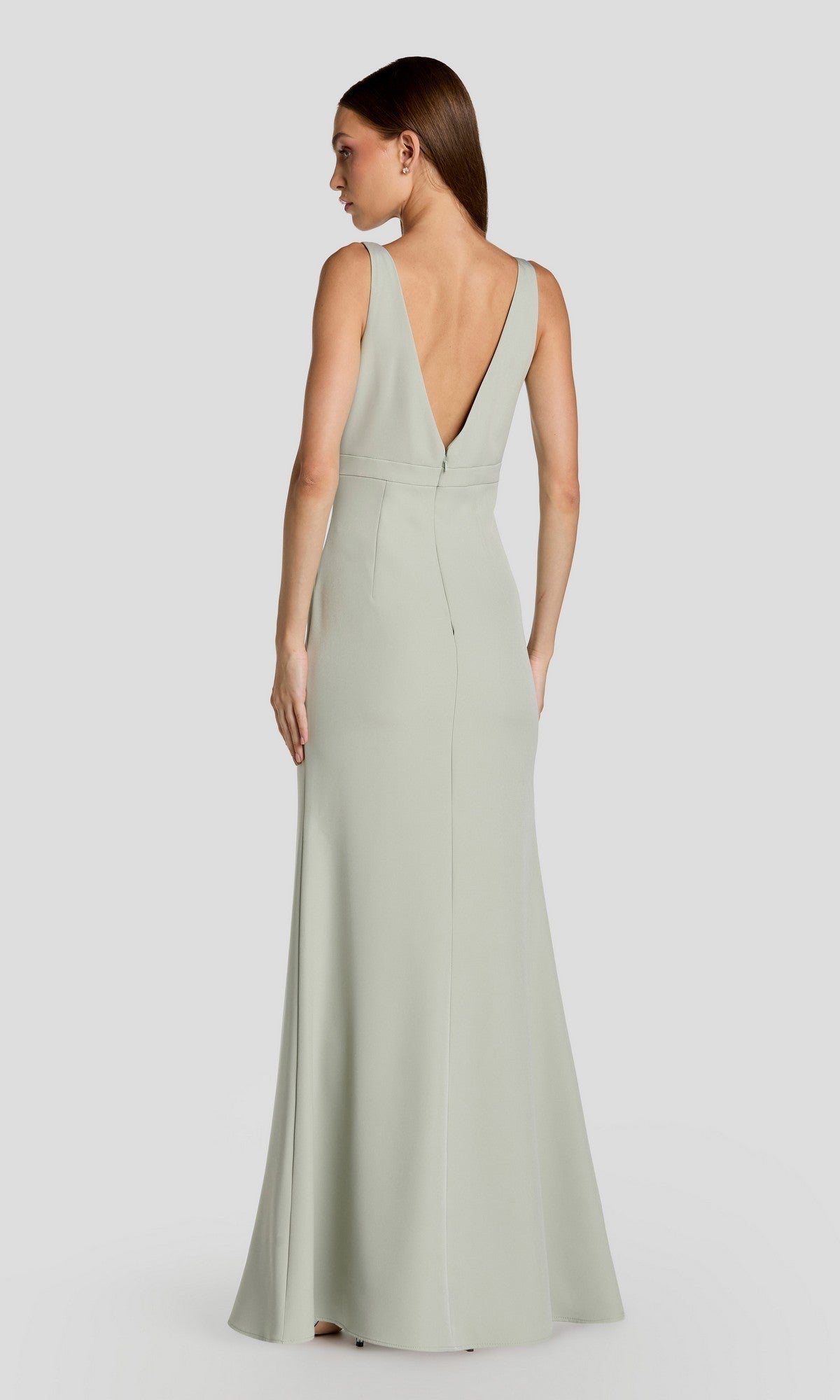 A woman models the Mac Duggal 2371 long formal dress, a sleeveless light green crepe gown with a deep V-back, standing against a plain light gray background.
